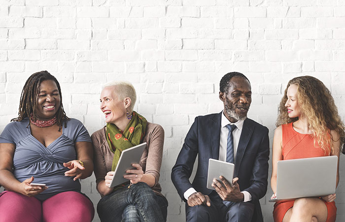 Coworkers sitting on a bench sharing content on an assortment of devices.